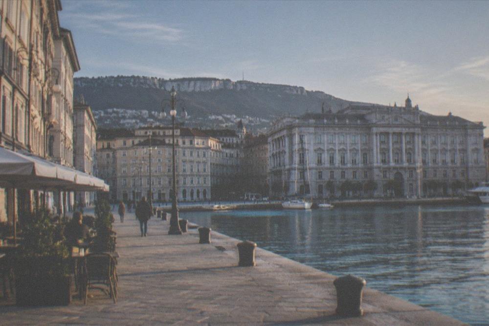 A grand seafront square with ornate facades opening onto a harbour at dusk