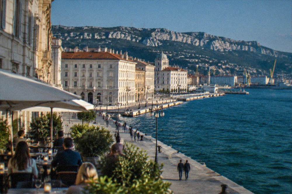 Outdoor evening tables along the Trieste seafront with the lit waterfront and dark sea behind
