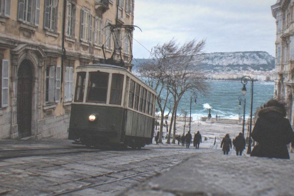 A vintage tram climbing a hillside street above Trieste with the sea behind