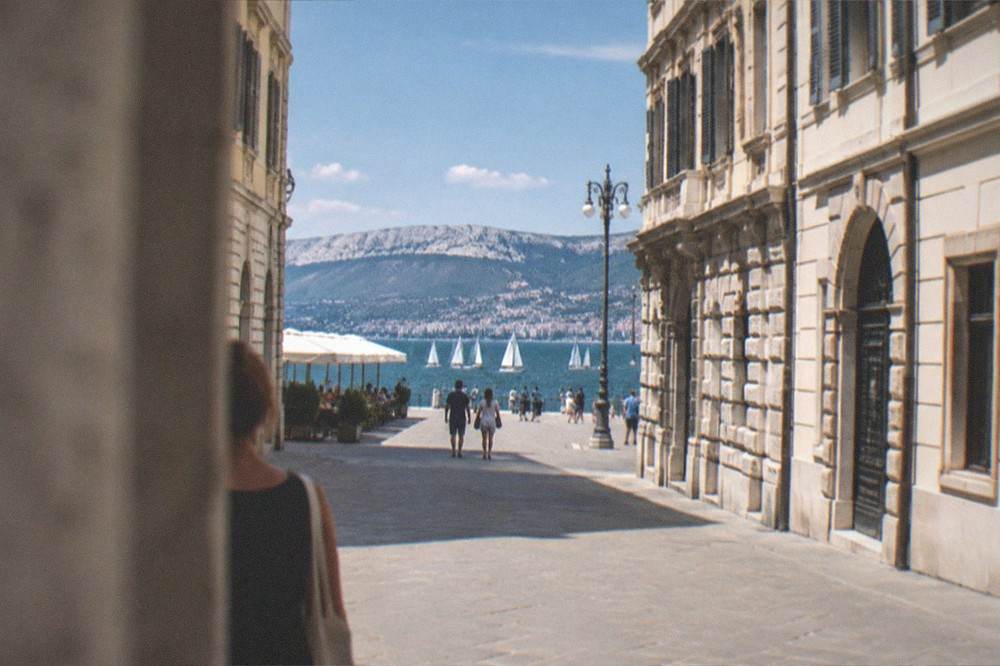 White sails spread across the Gulf of Trieste seen from the stone seafront by the grand square
