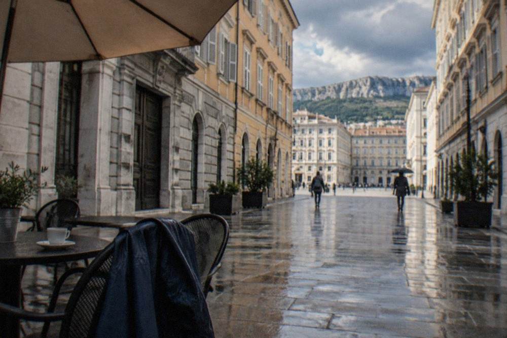 An umbrella and rain jacket on a café table beside a rainy street in Trieste
