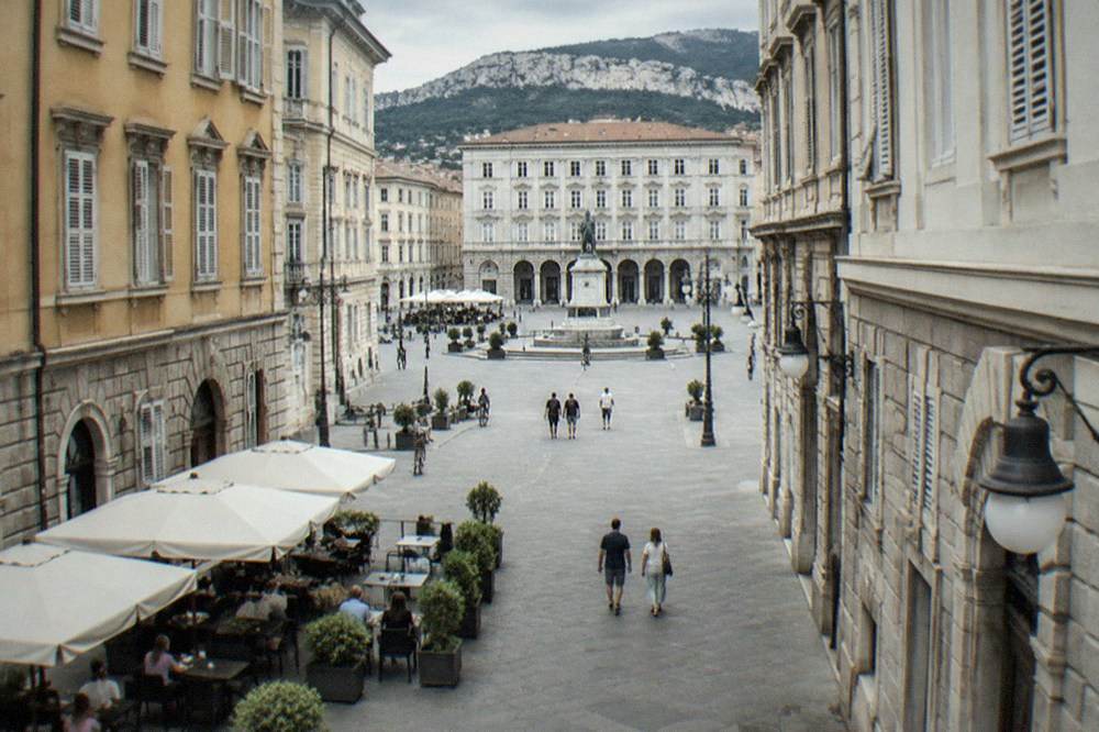 People eating outdoors at a pavement table in a Trieste square in warm weather