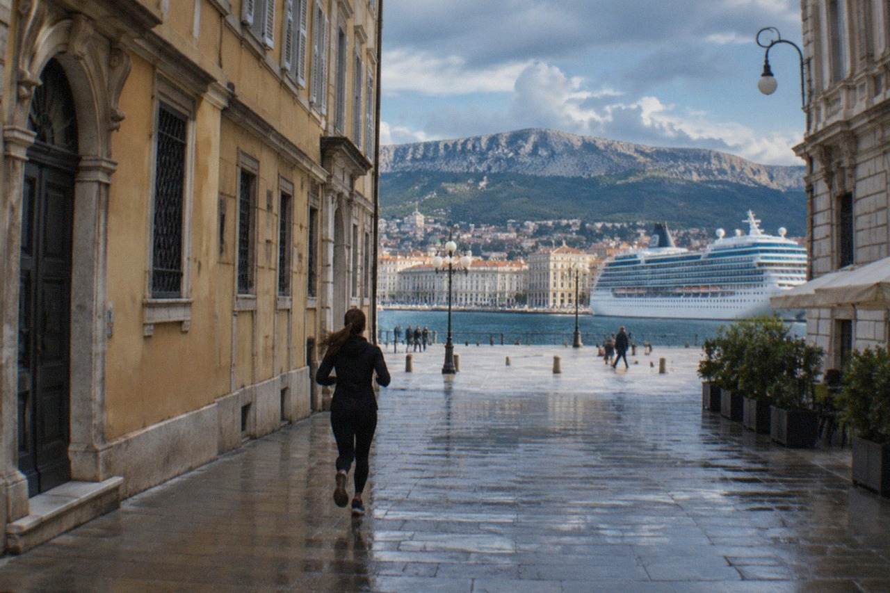A cruise ship docked at the Trieste cruise terminal with the city's waterfront buildings behind it