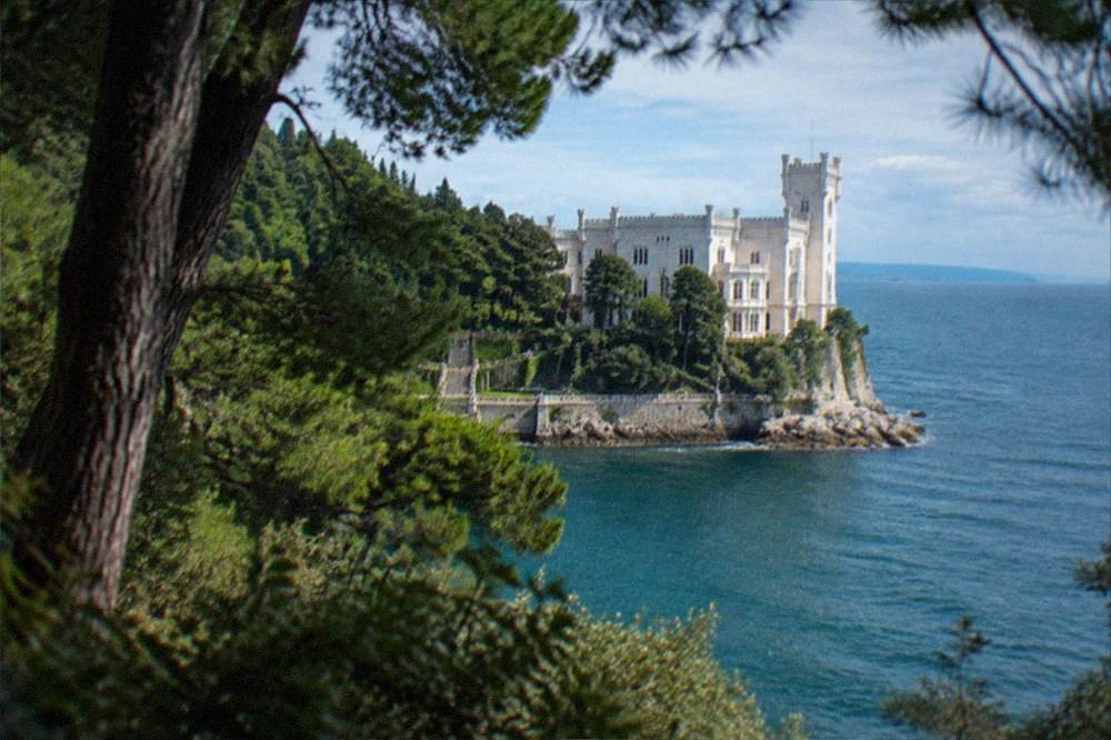 White cliff-top Miramare Castle above the Adriatic seen through trees