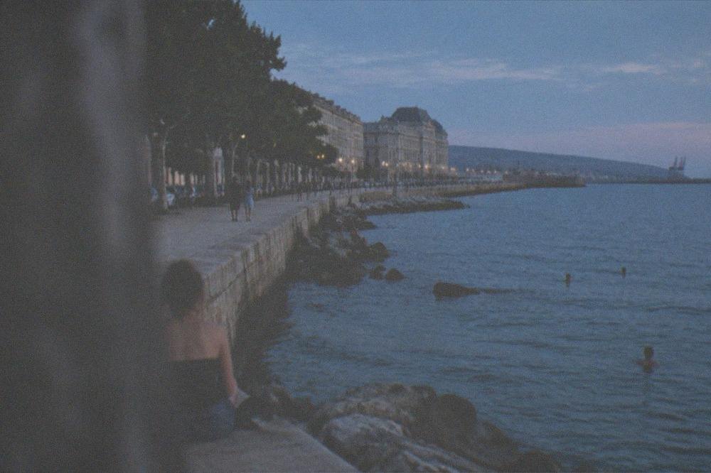 A rocky seafront promenade with people swimming in the Adriatic below