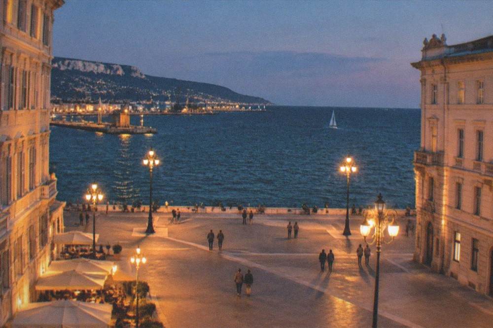 An evening view of a lit seafront square with the dark sea beyond