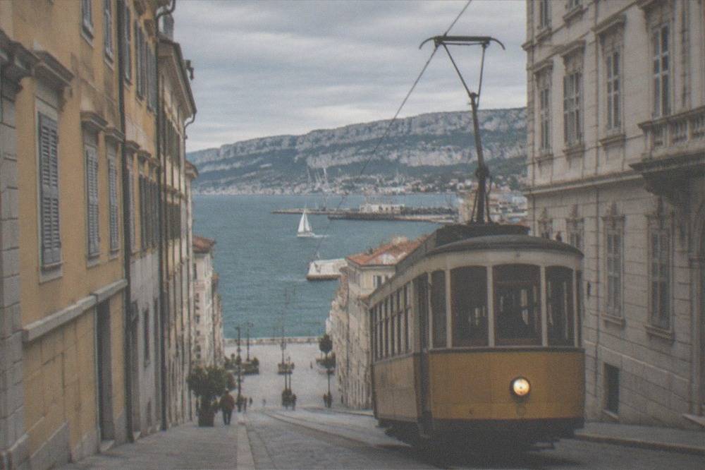 A vintage tram climbing a hill above a coastal city with the sea behind