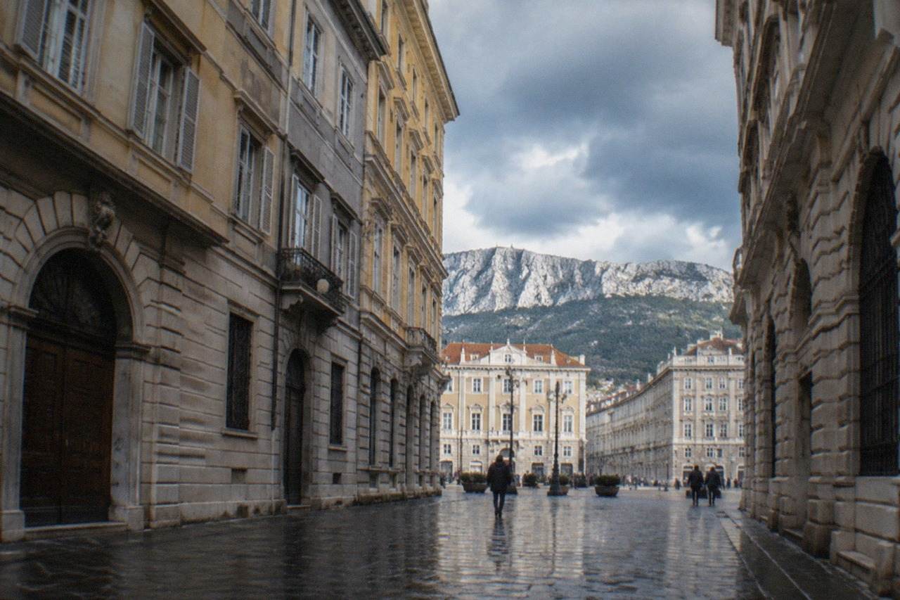 Wet cobblestones and grand Habsburg-era facades in central Trieste under grey skies