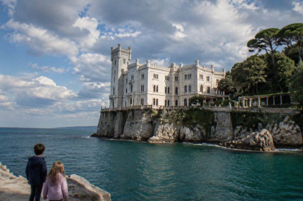 Children looking up at the facade of Miramare Castle above the sea