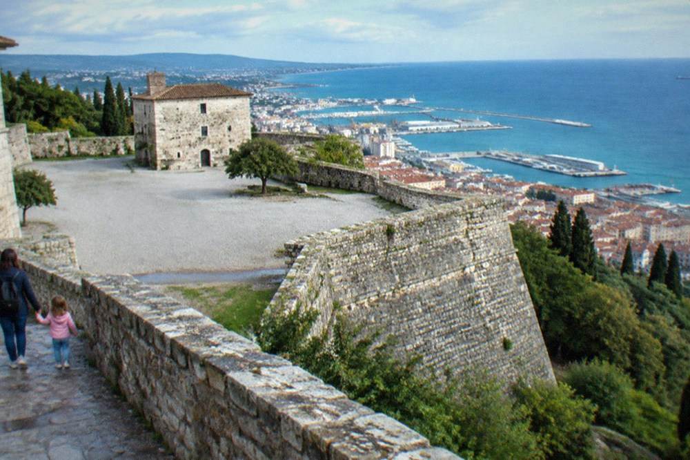 A child holding a parent's hand on the stone walls of San Giusto Castle