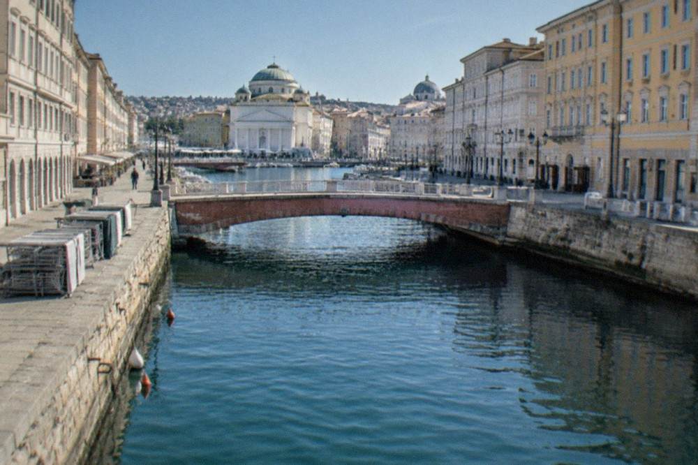The Grand Canal of Trieste crossed by the red Ponte Rosso bridge with church domes behind
