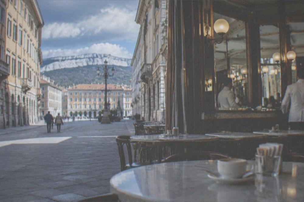 A historic Trieste cafe interior with marble tables, mirrors and waiters in white jackets