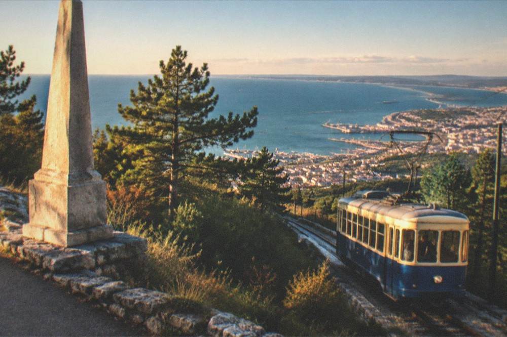 The vintage blue and cream Opicina tram on a hillside track above Trieste with the gulf in the distance